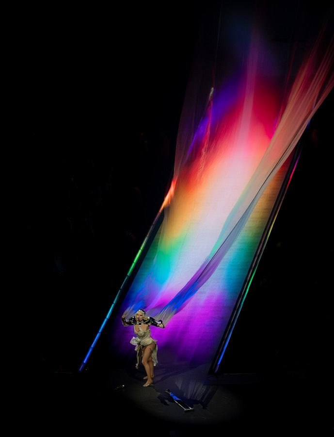 Gaga podczas trasy Mayhem Ball w 2025 roku, z tęczowym światłem rzucanym na jej długą białą pelerynę
