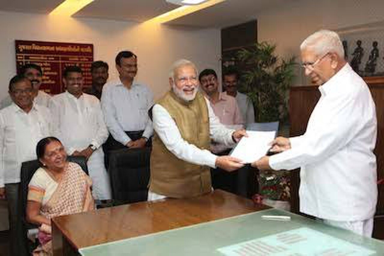 Modi überreicht dem Sprecher Vajubhai Vala der Gujarat Vidhan Sabha seinen Rücktritt als Abgeordneter von Maninagar; im Hintergrund ist Ministerpräsidentin Anandiben Patel zu sehen