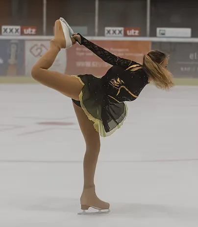 Eiskunstläuferin in schwarz-goldenem Wettkampfkleid in einer Standwaage, den Schlittschuh über dem Kopf gefasst