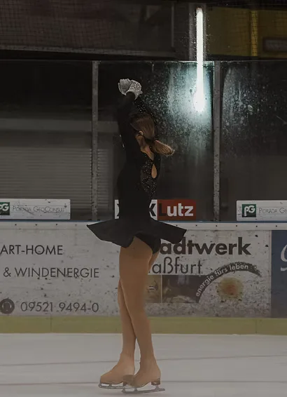 Eiskunstläuferin in schwarzem Kleid mit erhobenem Arm am Ende ihrer Kür in der Eishalle Haßfurt