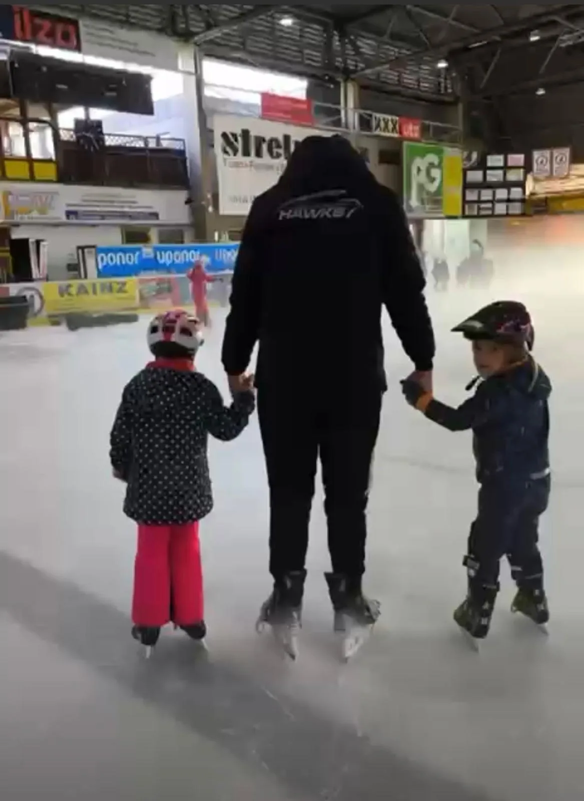 Trainer hält zwei Kinder der Laufschule an der Hand auf dem Eis