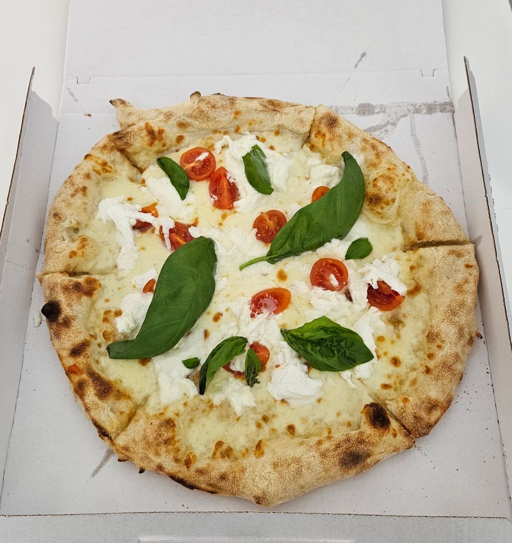 Pizza with crispy crust topped with mozzarella, cherry tomatoes, and fresh basil leaves in a white pizza box.