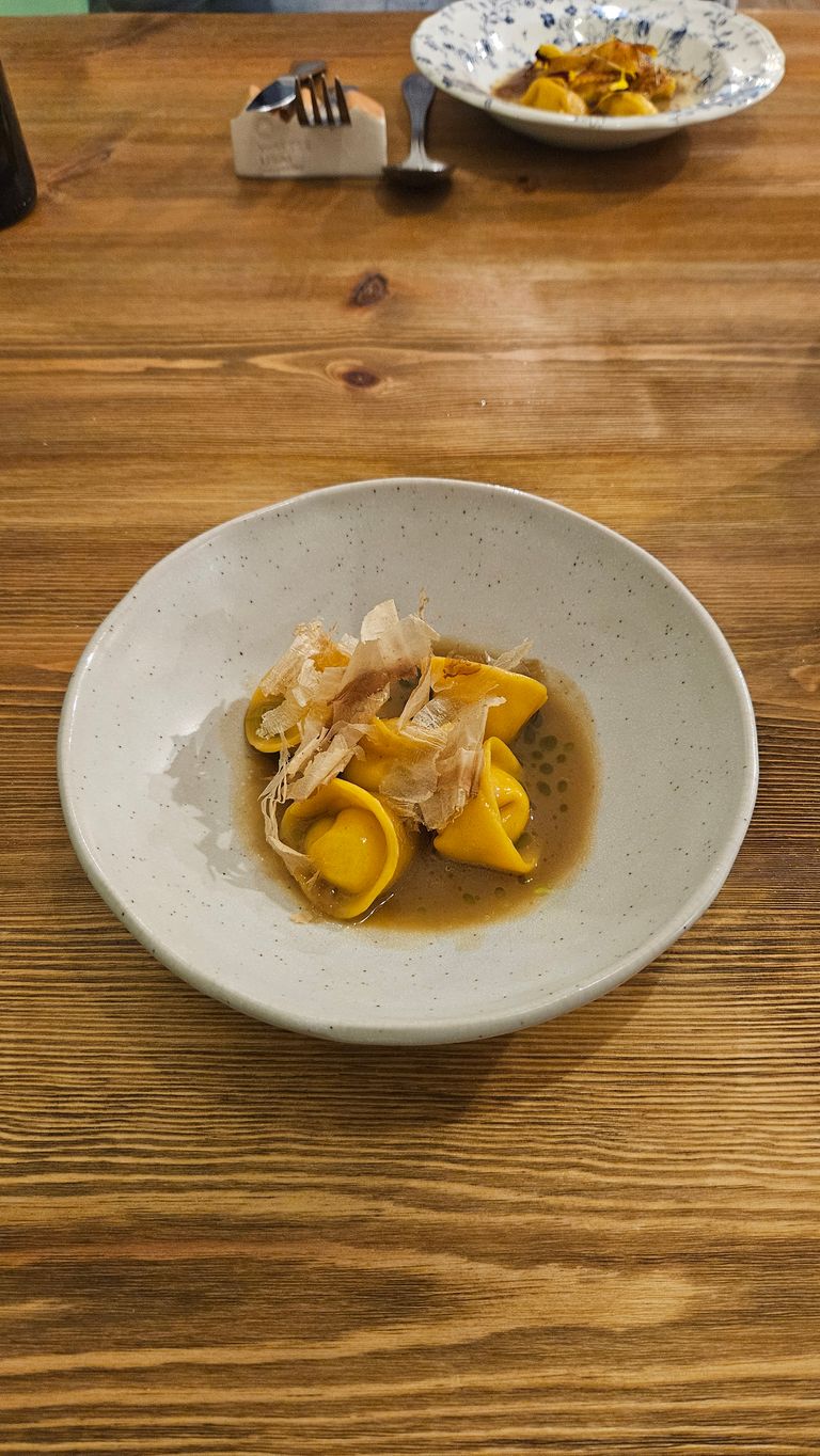 Teller mit mehreren gefüllten Tortellini in einer klaren Brühe auf einem Holztisch.