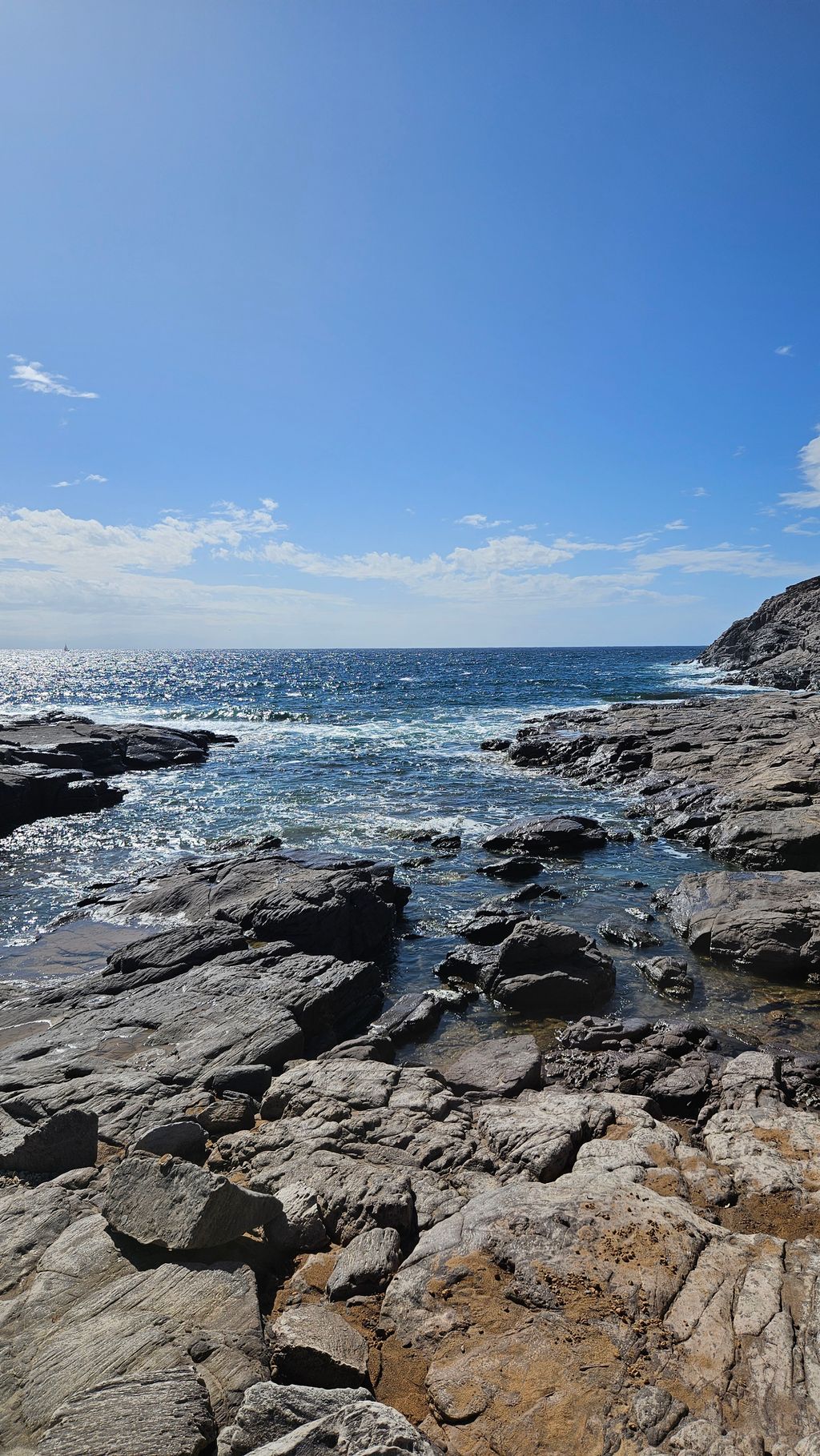 Felsige Küste mit Wellen, die gegen die Felsen schlagen, unter einem klaren, blauen Himmel.