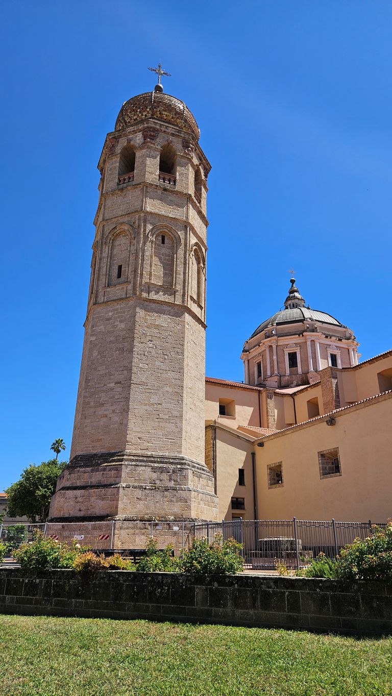 Turm mit einer goldfarbenen Kuppel und Kreuz an der Spitze vor einem Gebäude mit einer großen Kuppel und klar blauem Himmel.