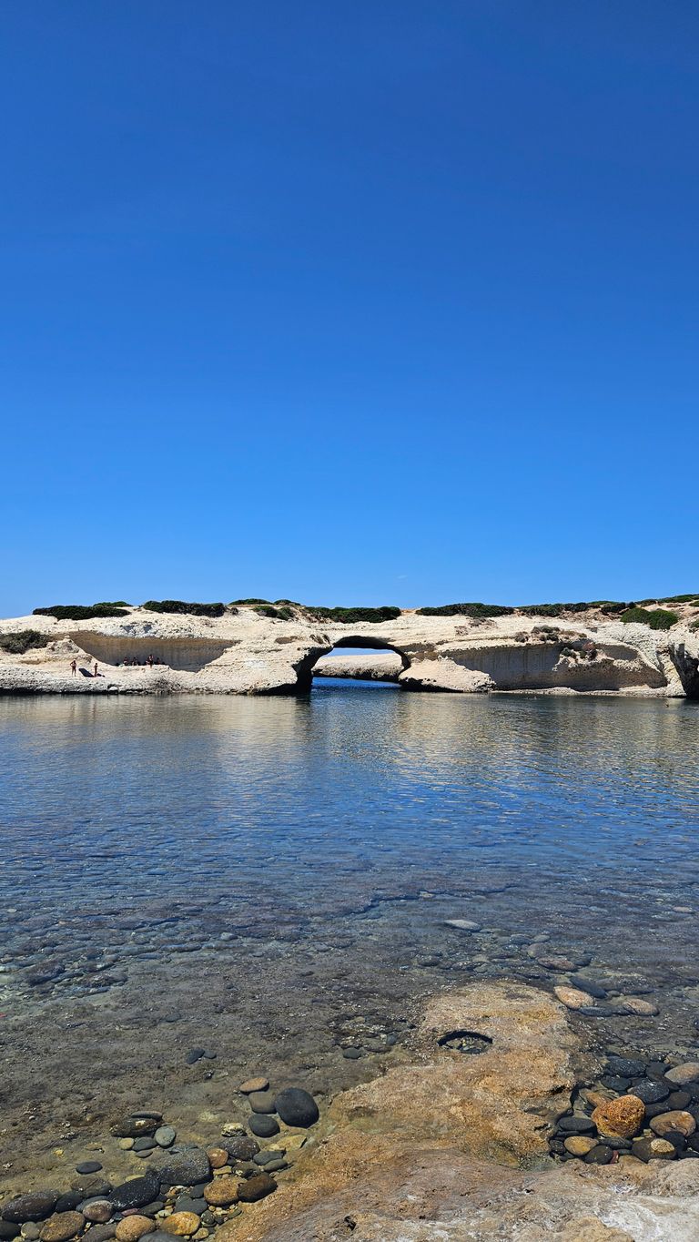 Natürliche Felsformation mit einem Bogen über klarem Wasser unter einem wolkenlosen blauen Himmel.