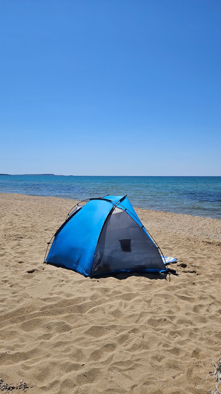 Zelt am Sandstrand mit Blick auf das ruhige Meer unter einem klaren blauen Himmel.