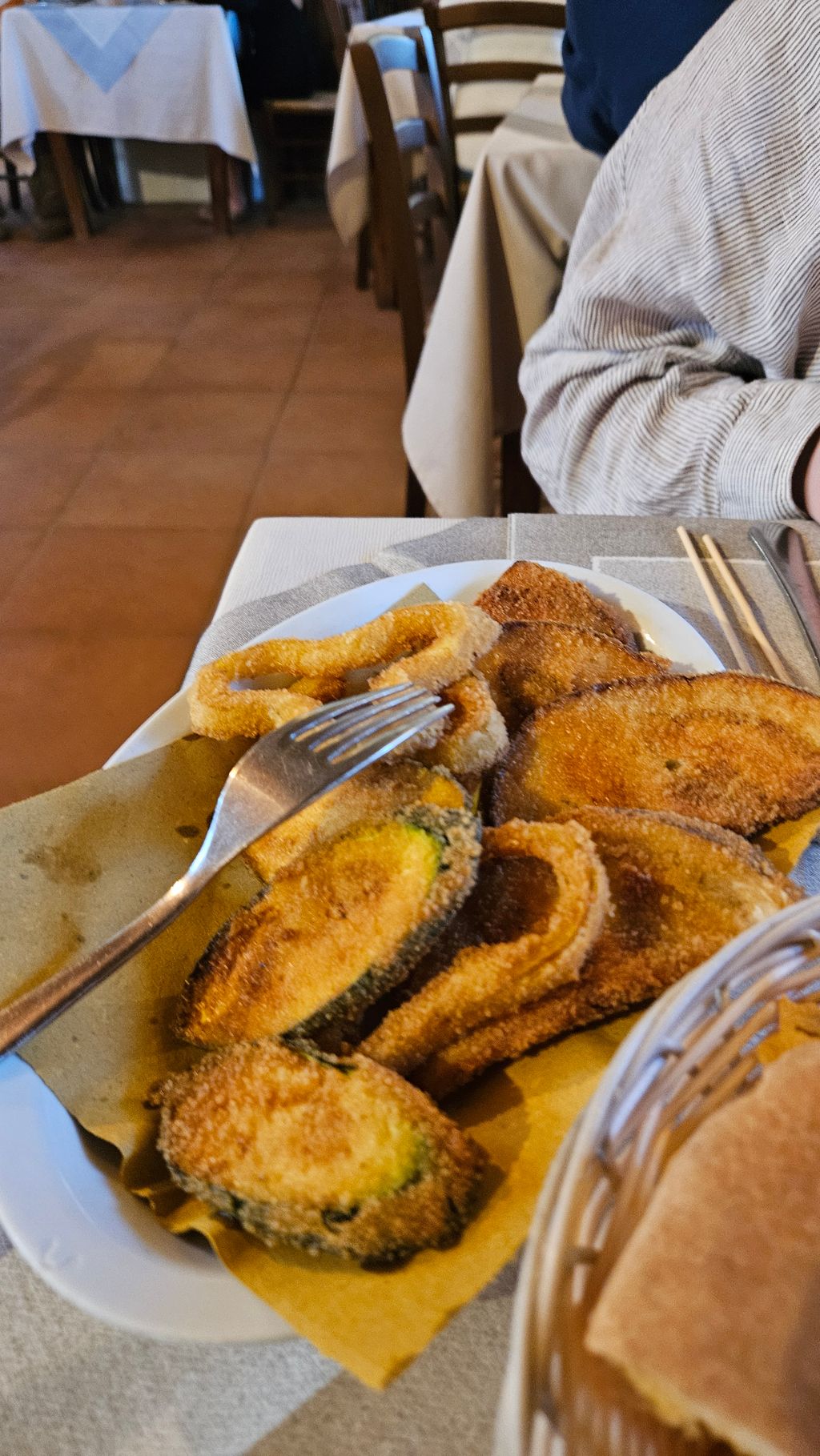 Teller mit panierten gebratenen Gemüsescheiben und einem Metallgabel darauf in einem rustikalen Restaurant mit mit karierten Tischdecken.