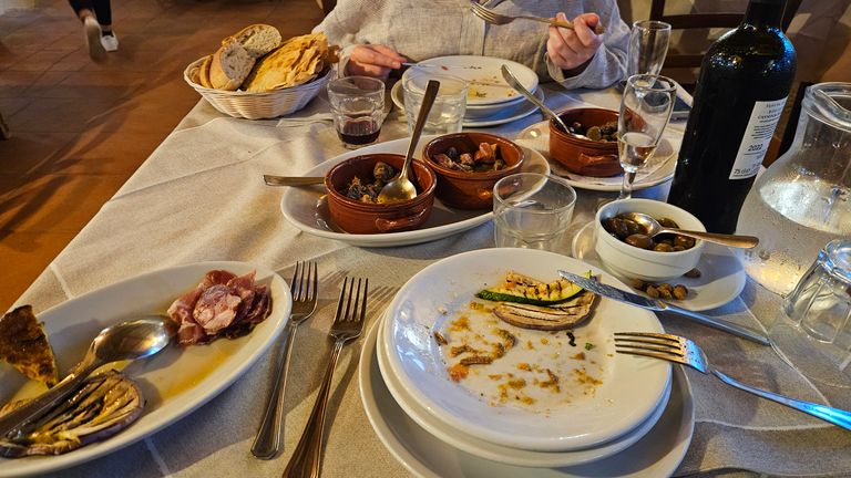 Reste einer Mahlzeit auf Tellern und Schüsseln auf einem gedeckten Tisch mit Besteck, einem Korb mit Brot, Gläsern und einer Flasche Wein in einem Restaurant.