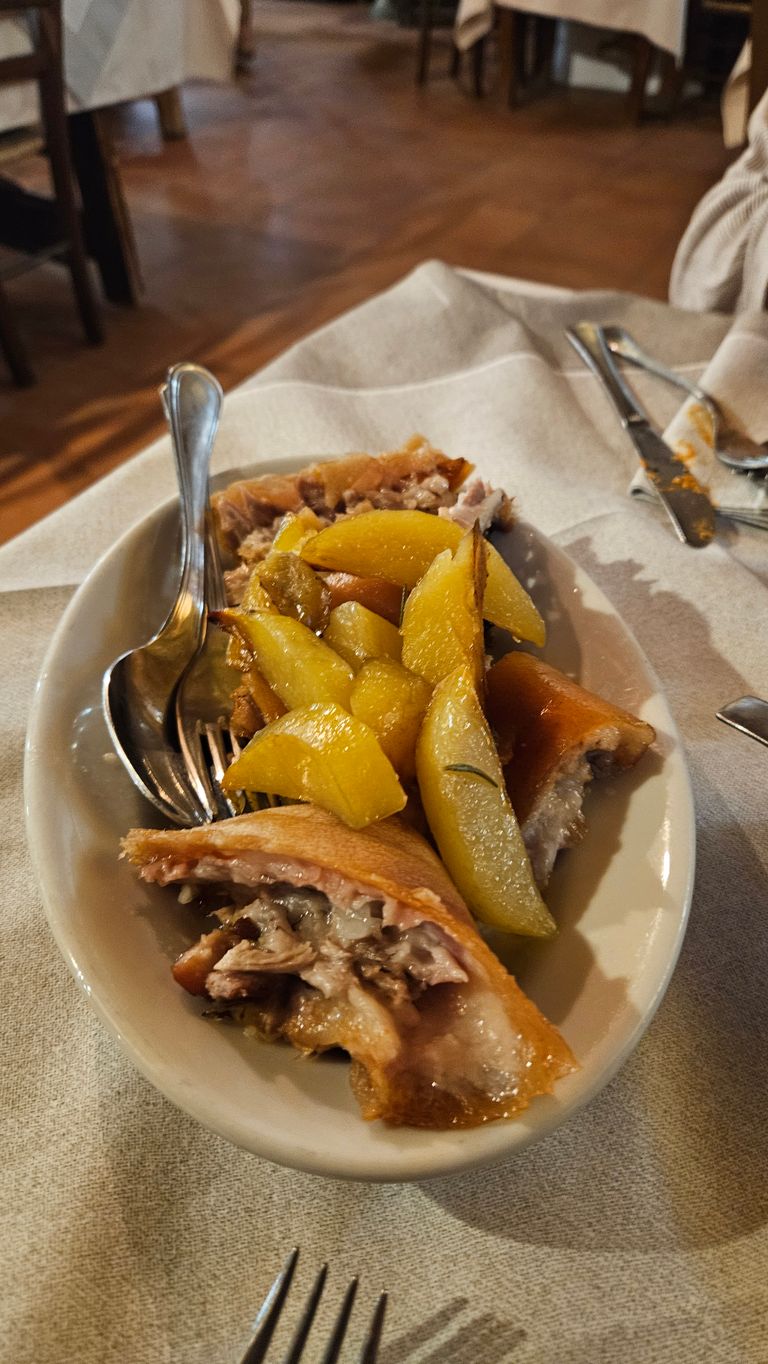Servierteller mit gebratenen Kartoffelspalten und gebratenem Fleisch auf einem Tisch mit beige-grauem Tischdecke in einem Restaurant.