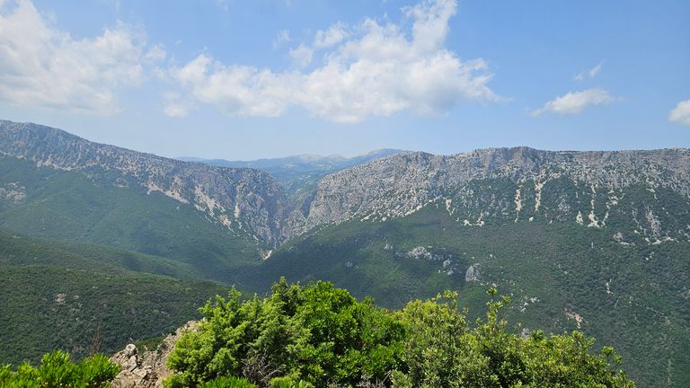 Berglandschaft mit grünen Hügeln und Felsen unter einem teilweise bewölkten blauen Himmel.