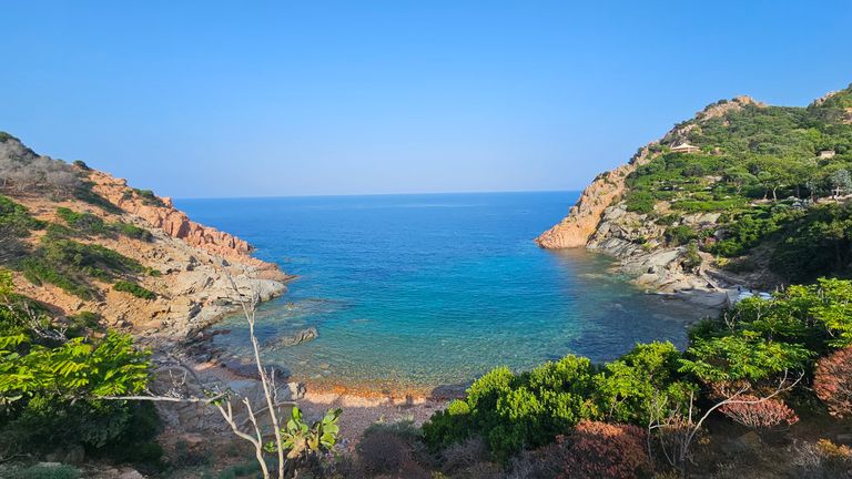 Eine ruhige Bucht mit klarem, blauem Wasser, umrahmt von felsigen Hügeln und grüner Vegetation unter klarem Himmel.