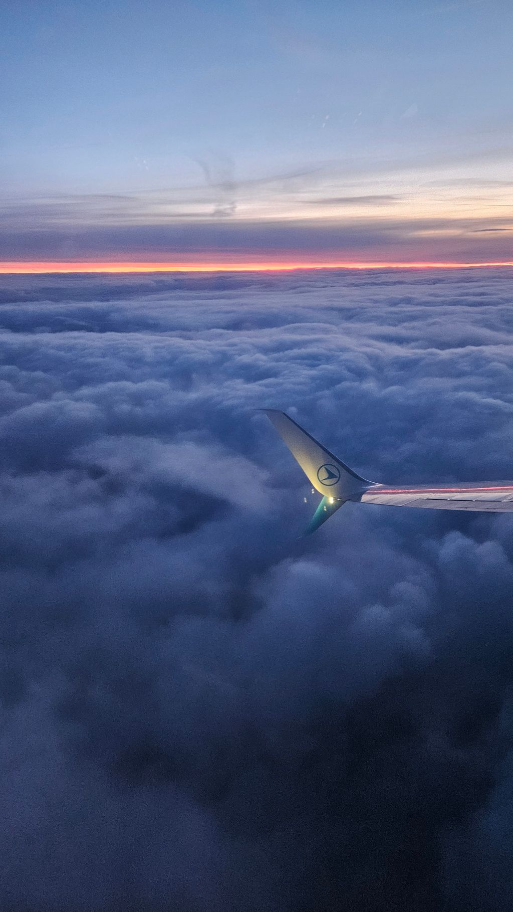 Airplane wing above a cloud layer during twilight with an orange strip on the horizon.