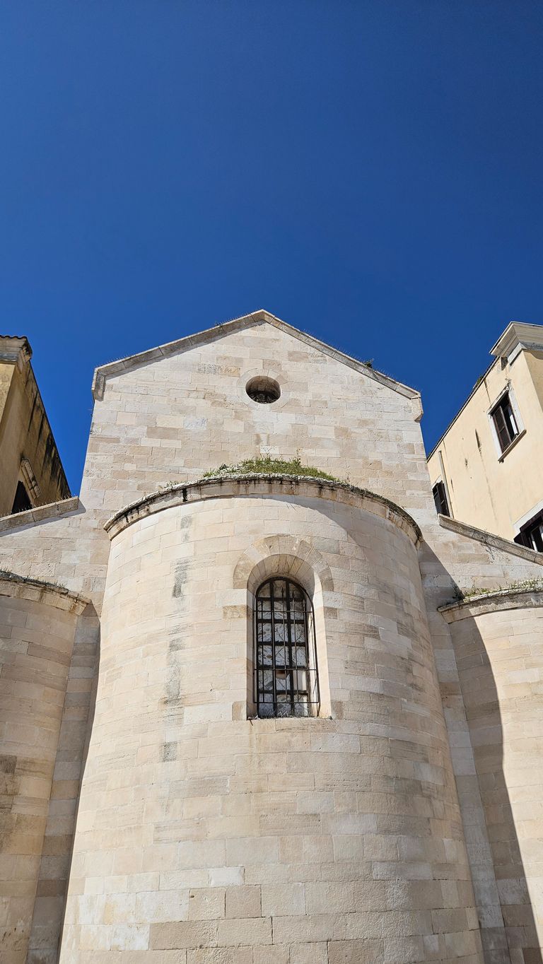 Facade of a historic building with yellowish-white masonry and a pointed roof under a clear blue sky.