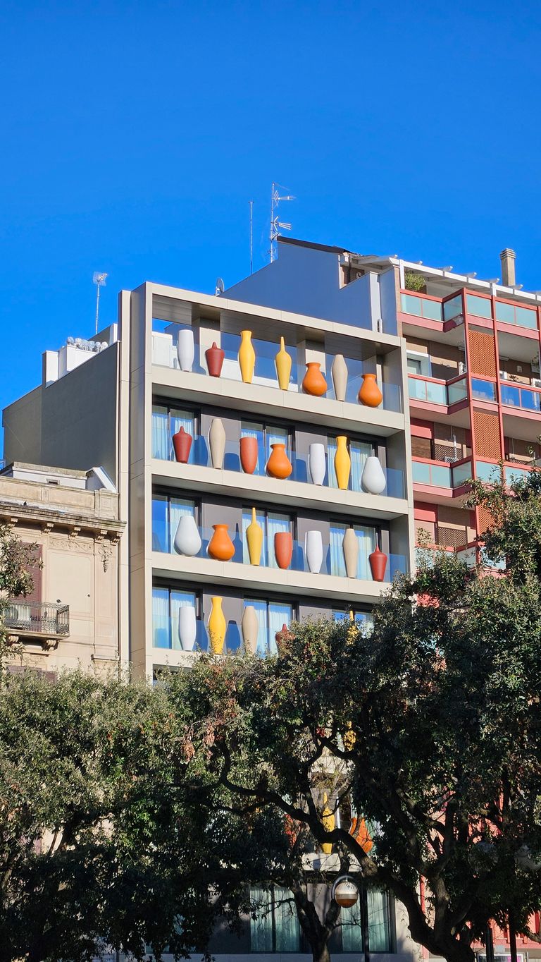 Multi-story building with several large colorful vases on the balconies, surrounded by trees and other buildings under a clear blue sky.