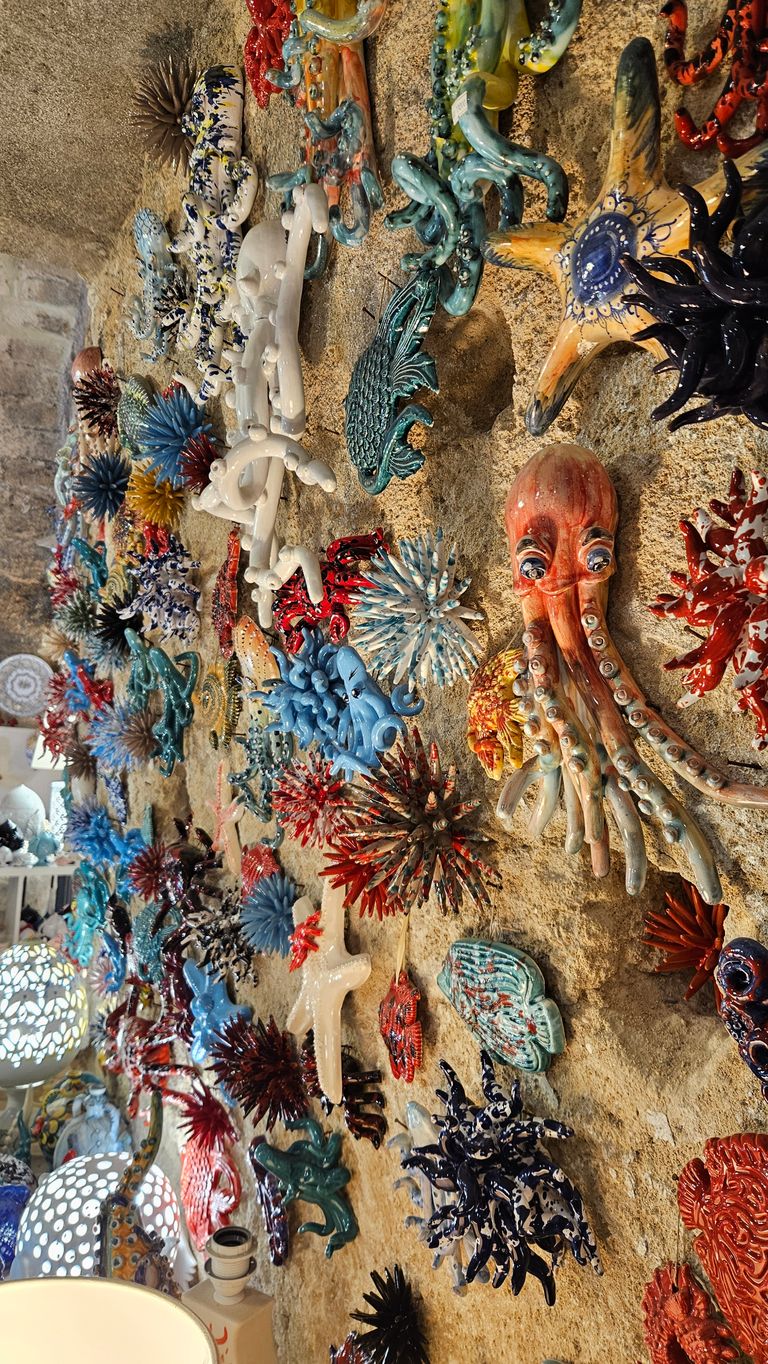 Colorful ceramic sea creatures and corals mounted on a rough stone wall, including a red octopus and an orange-yellow starfish.