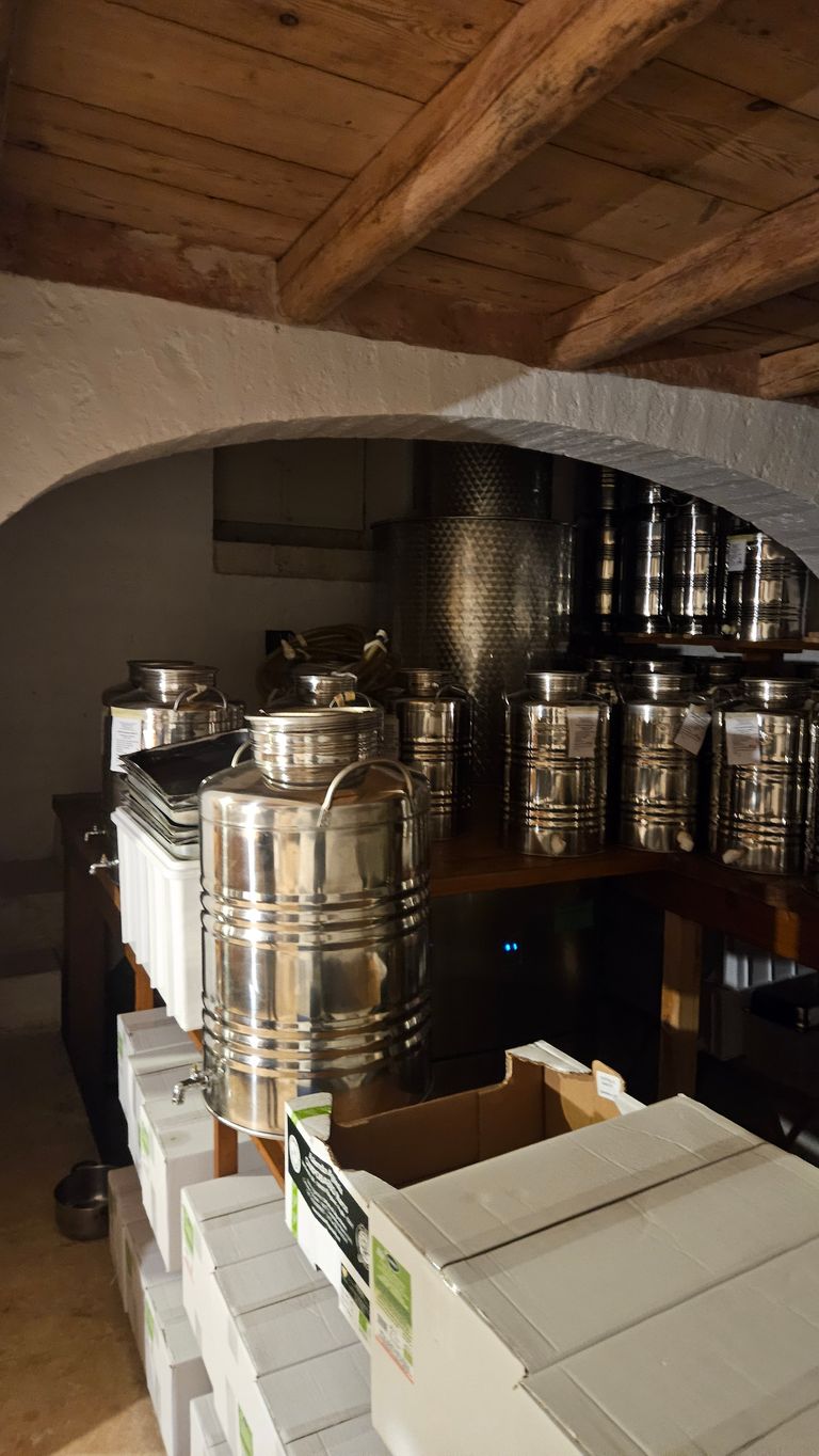 Several shiny stainless steel tanks on a wooden table in a room with whitewashed walls and wooden ceiling, with stacked white cartons in front.