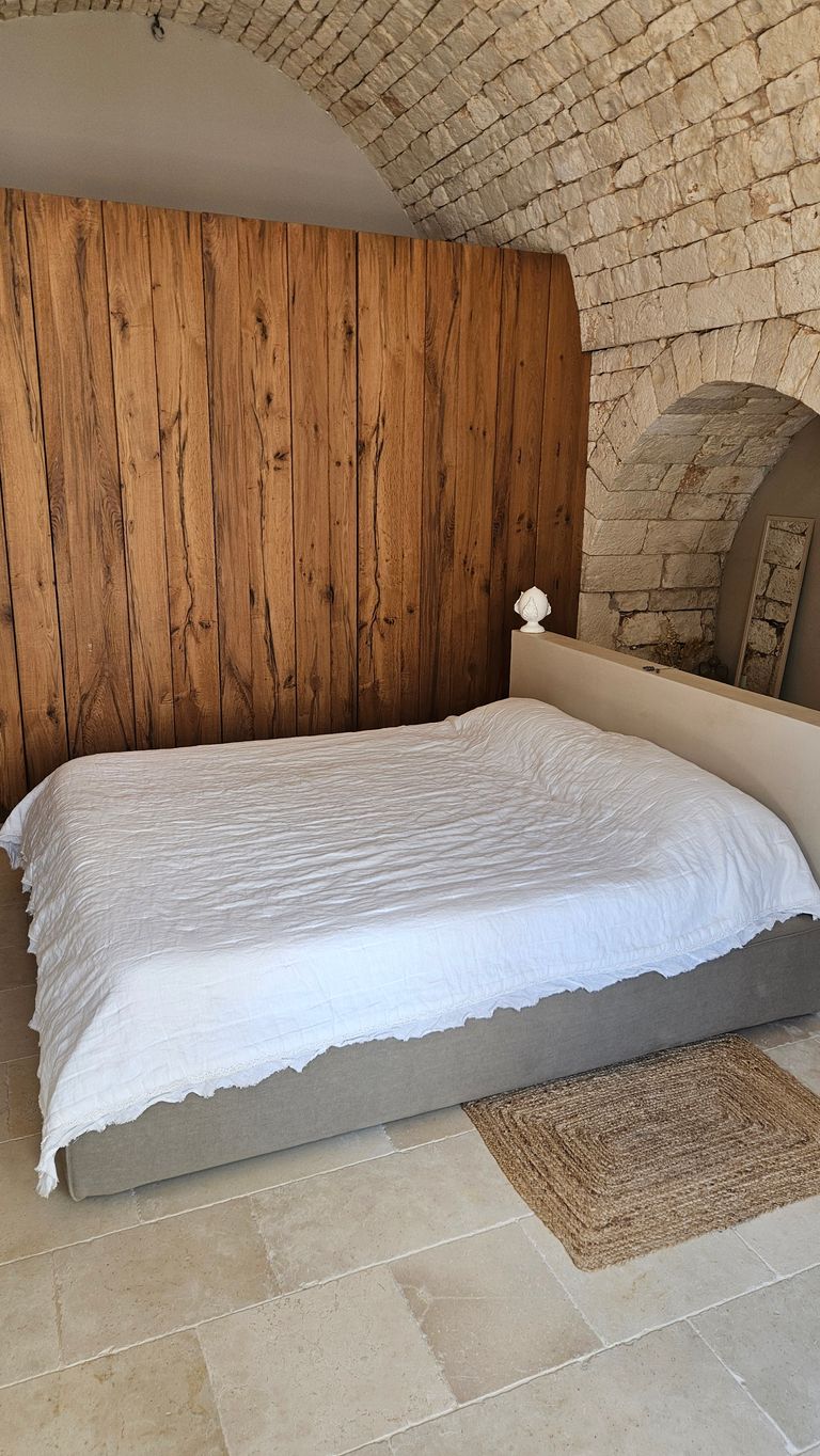 Cozy bed with white bedspread in front of wooden paneling and stone arch wall in a bright room.