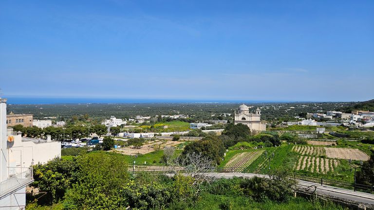 View of a rural area with fields, scattered buildings, and a church under a clear blue sky.