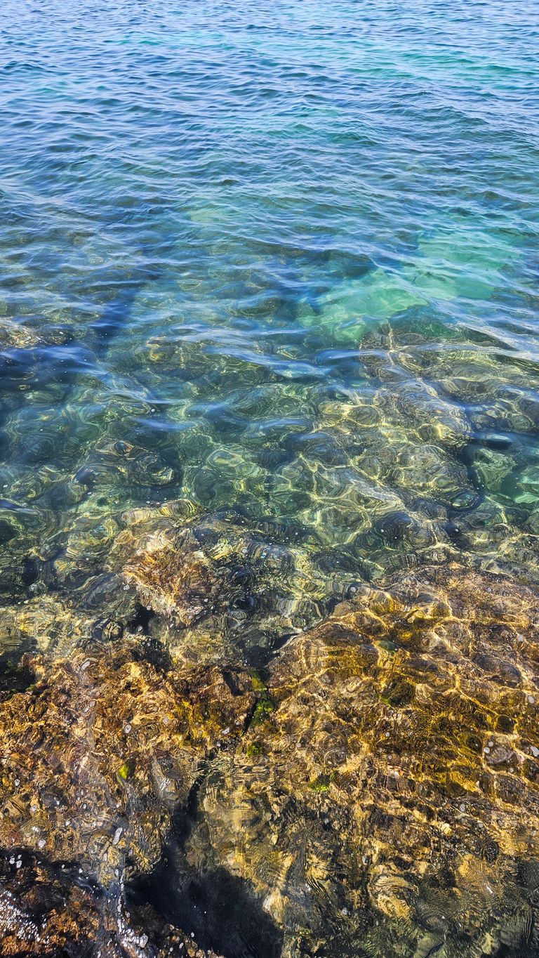 Clear seawater with visible rocks and stones on the bottom under sunny conditions.