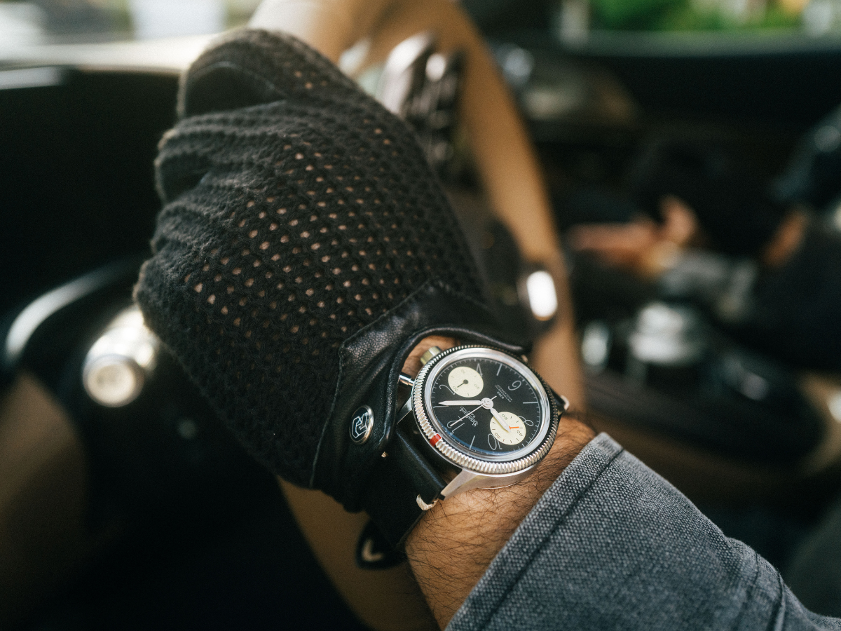 Edelstahl-Chronograph mit schwarzem Zifferblatt und Lederband, getragen am Handgelenk mit schwarzem Fahrerhandschuh.