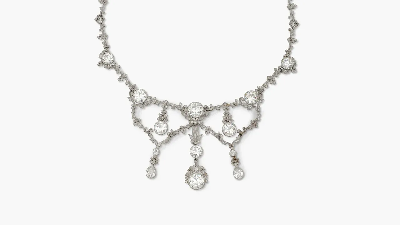Silbernes Diamantcollier im Girlandenstil mit runden und tropfenförmigen Steinen, mittig drei Anhänger, auf weißem Grund