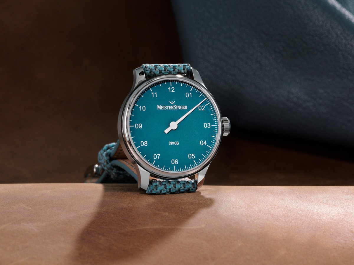 MeisterSinger №03 Special mit türkisblauem Zifferblatt und Textilband, vor Leder und Stoff in Szene gesetzt