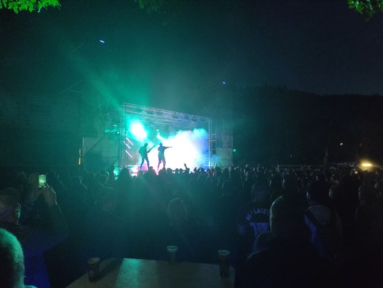 Bühne bei Nach. Viele bunte Lichter, Bühnennebel und die Silhouetten dreier Musiker auf der Bühne