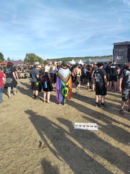 Festival Besucher auf dem Infield des Rock Harz von hinten. Einer trägt eine Regenbogenflagge über den Schulter n