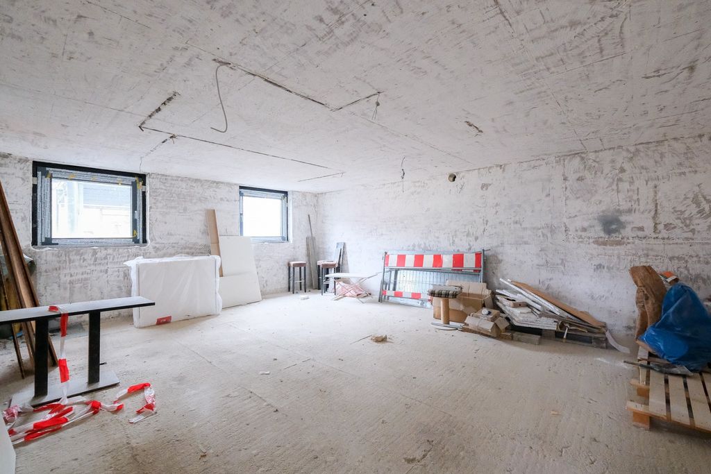 Empty unfinished basement room with exposed concrete walls, two small windows, and scattered construction materials.