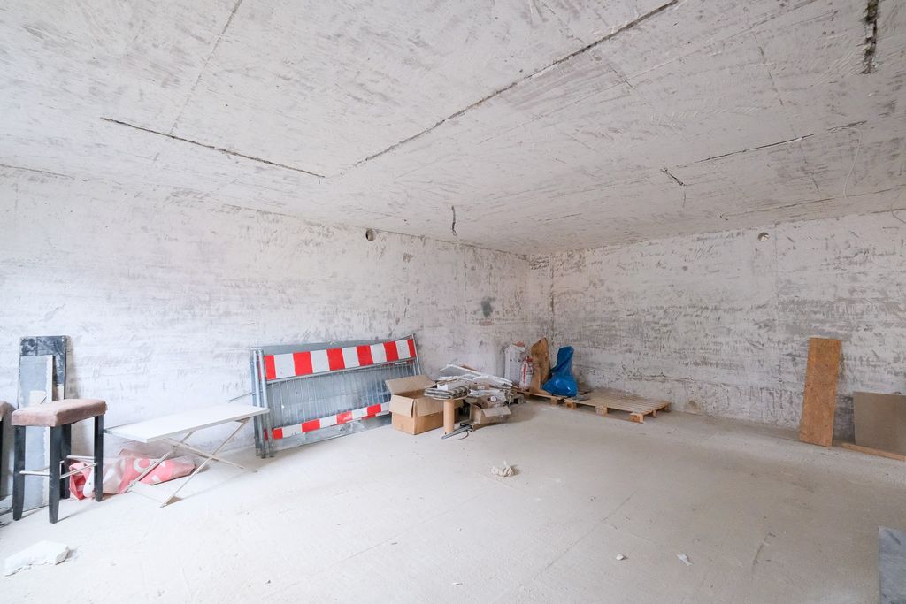 Empty, unfinished room with red and white construction barrier, cardboard boxes, and wooden pallets against one wall.