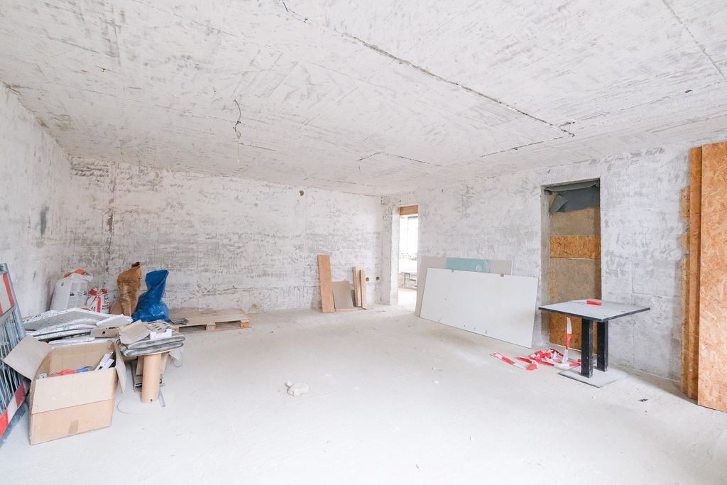 Empty room inside an unfinished or under-construction building with unplastered walls and construction materials in corners.