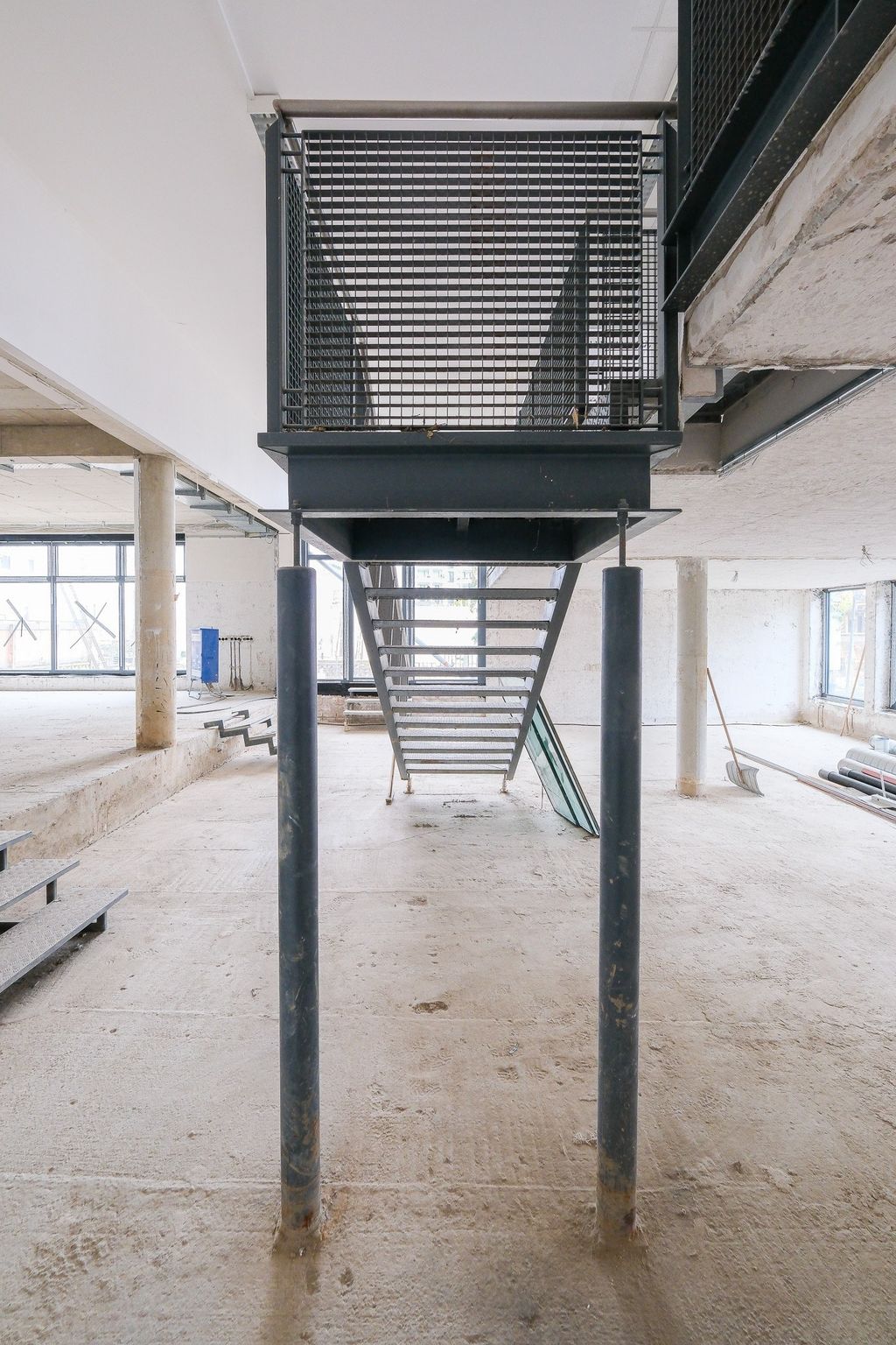 Industrial metal staircase in a large unfinished interior space with concrete floor and columns.