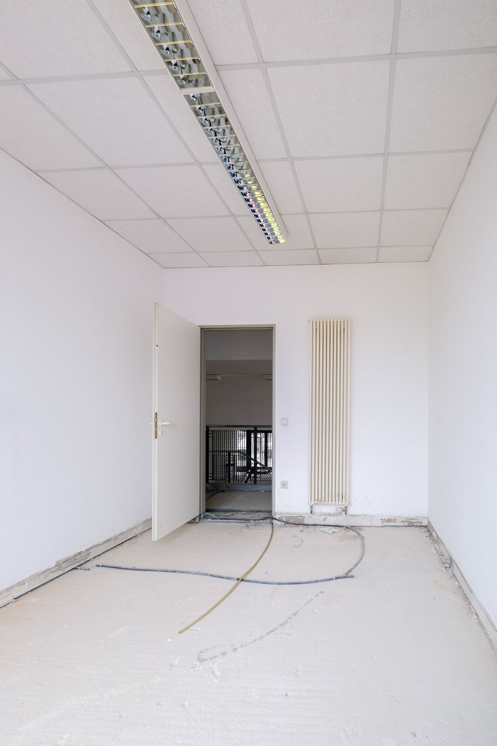 Empty room with white walls, ceiling light, and an open door leading to a darker adjacent area.