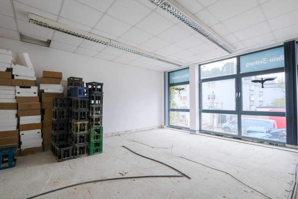 Empty room needing renovation with large windows and stacks of cardboard boxes and drink crates against one wall.