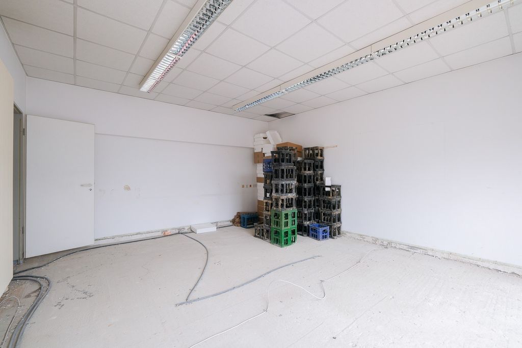 Empty room with white walls and ceiling, stacked plastic crates and some cardboard boxes in the corner, an open door on the left wall.
