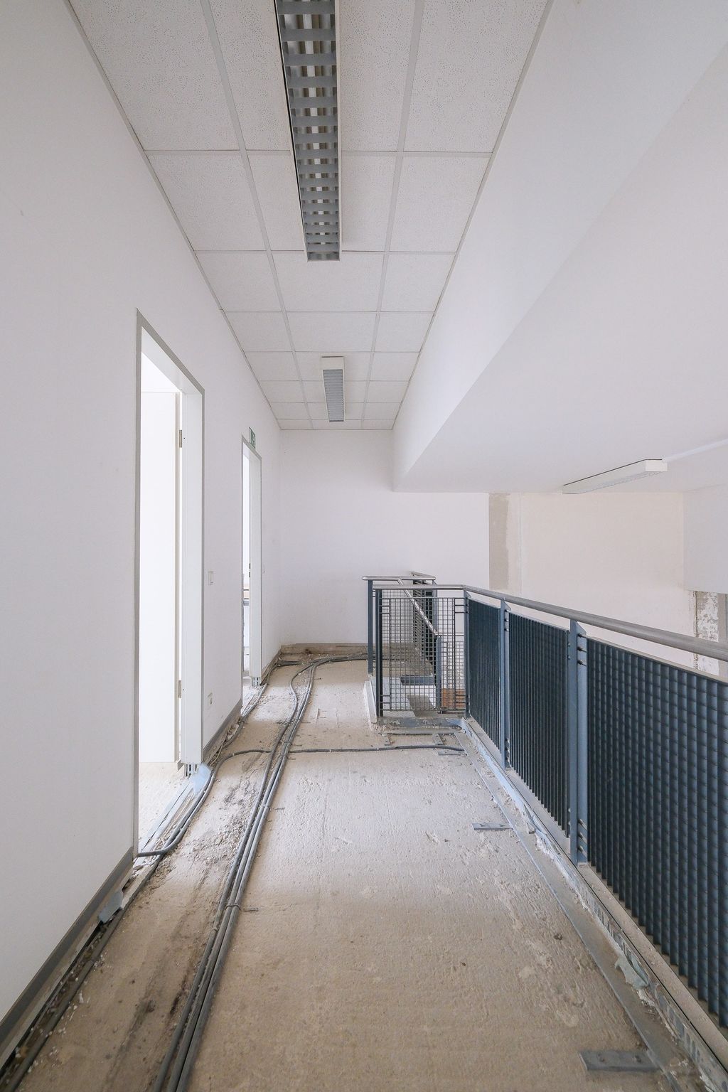 Hallway in an unfinished or under renovation building with exposed cables and a black metal railing along the right side.