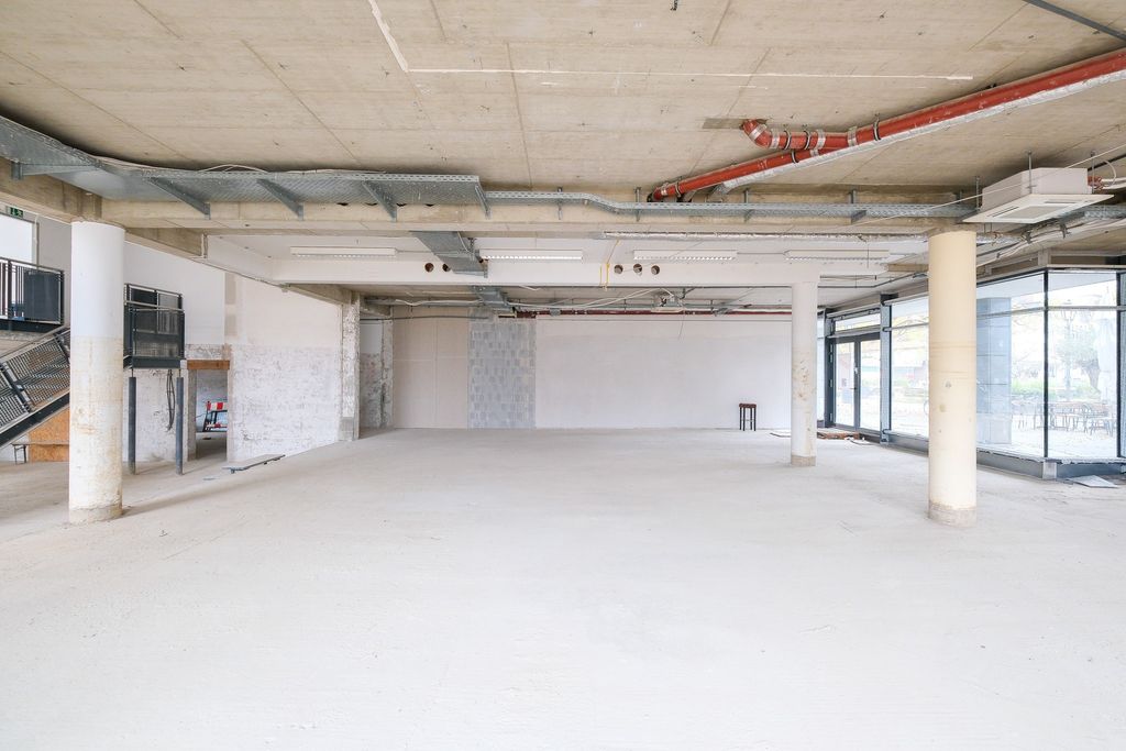 Empty, bright shell space with concrete columns, exposed piping, and large windows in a newly constructed building.