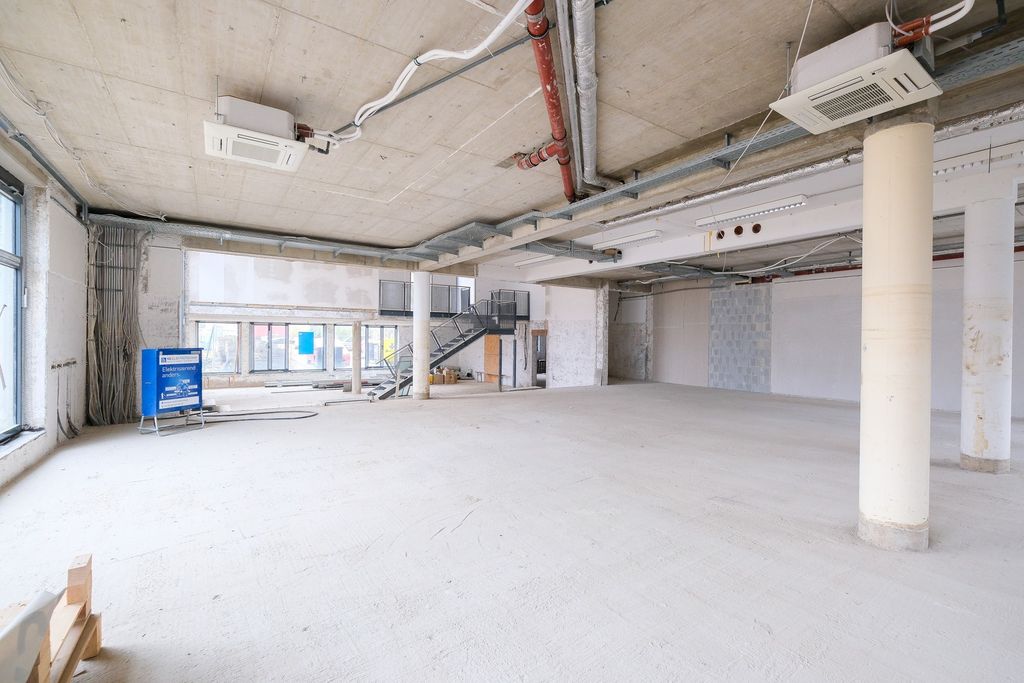 Large empty interior space of a construction site with exposed concrete ceiling, columns, and large windows.