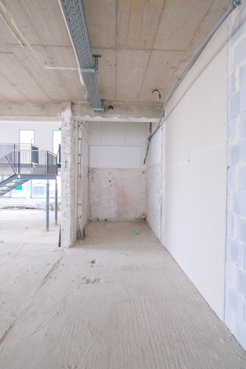 Interior shell construction with visible concrete floors, walls, and ceiling, partially equipped with cable trays and a staircase in the background.