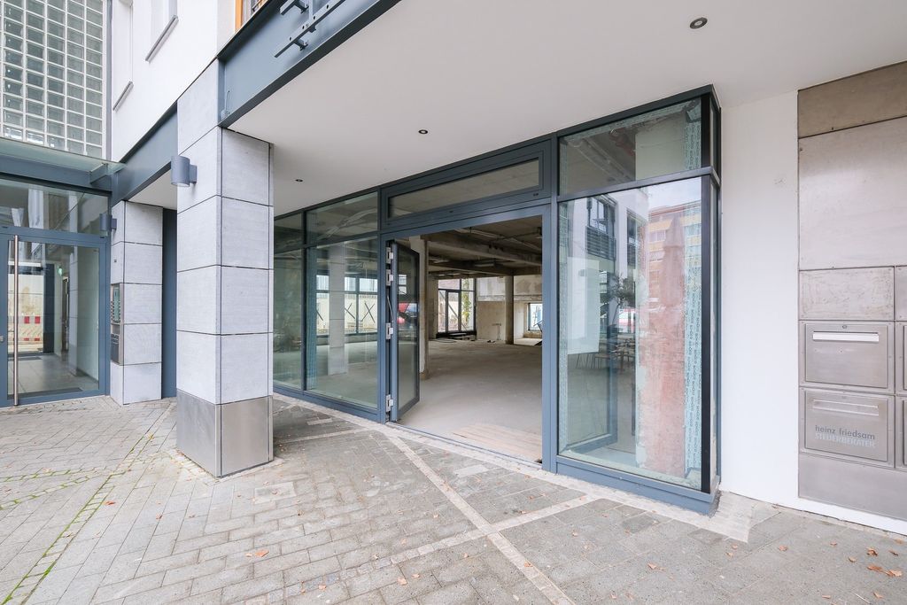 A modern storefront entrance with large glass windows and an open glass door leading to an empty, unfinished interior space.