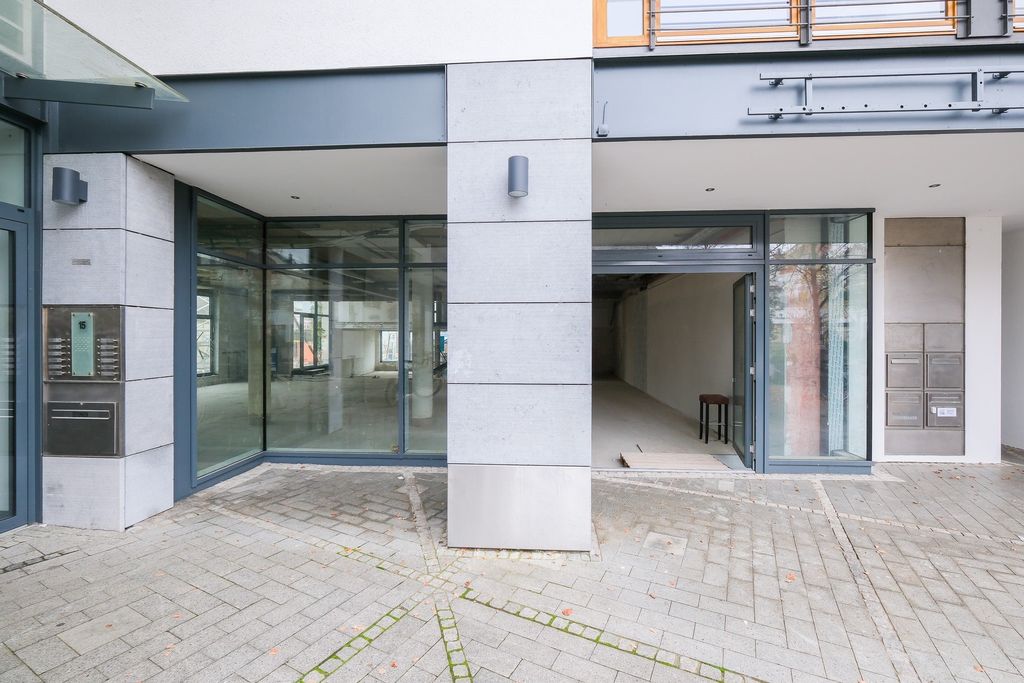 Modern building entrance with large glass windows and an open door revealing a room with a chair inside.