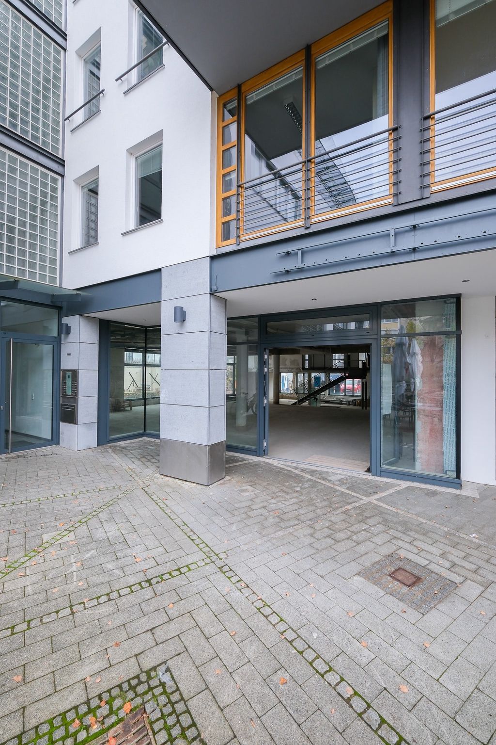 Entrance area of a modern building with large glass surfaces and gray paving stones.