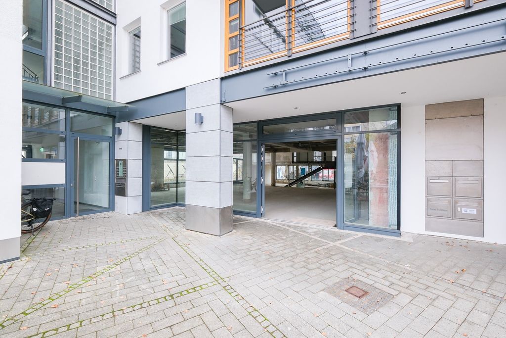 Modern entrance with large glass door and bright walls, paved floor in front and mailboxes to the right.