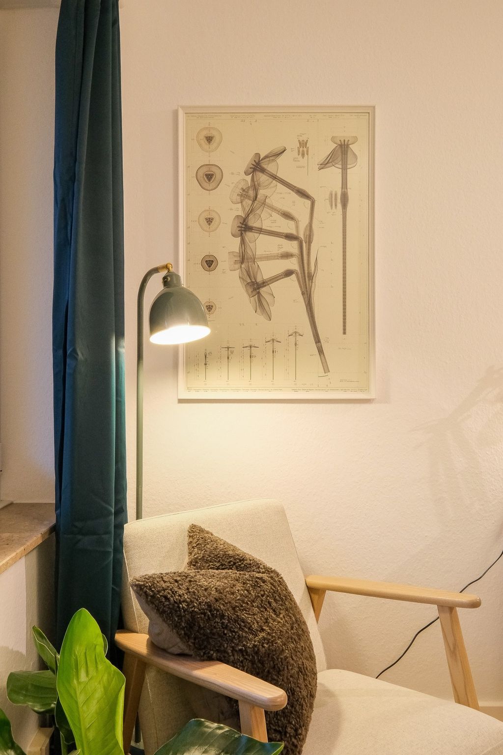 A cozy armchair with two brown cushions next to a green floor lamp and a large botanical poster on the wall.