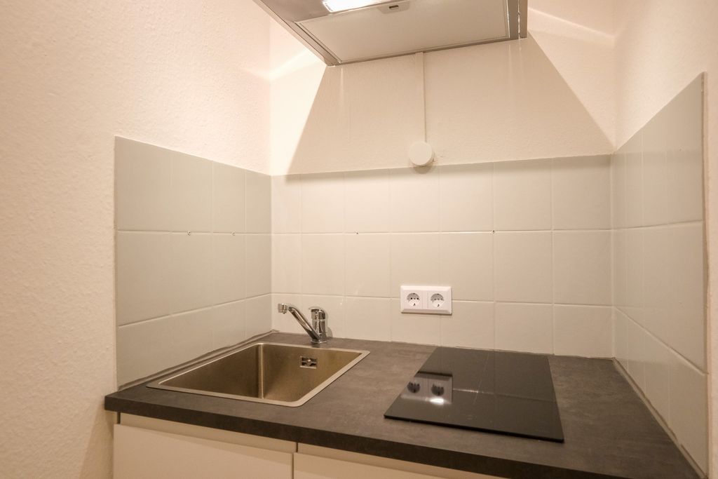 Compact kitchen counter with stainless steel sink, ceramic cooktop, and white tiled backsplash.