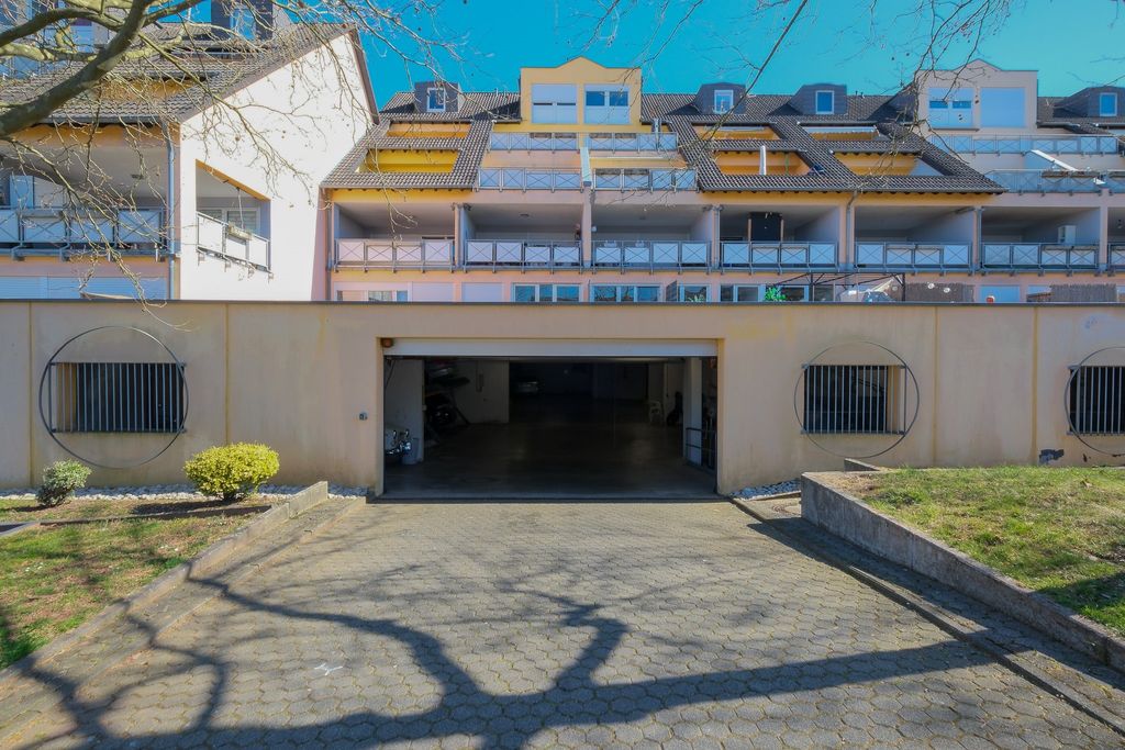 Entrance to an underground garage in front of a multi-story residential building on a sunny day with visible tree branches casting shadows on the ground.