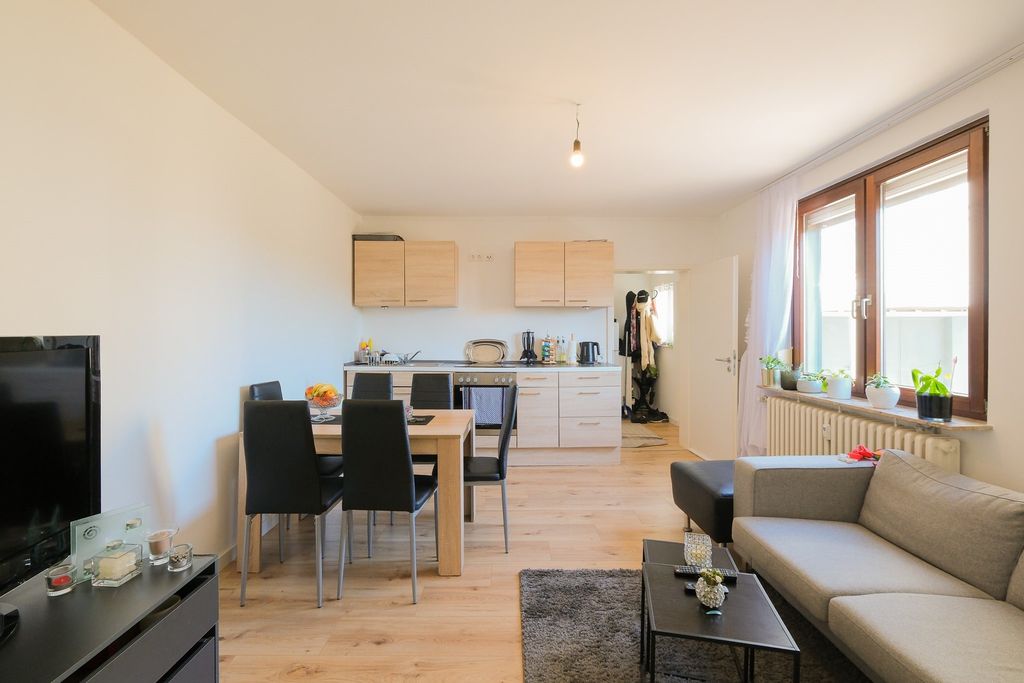 Cozy living and dining area with kitchenette, dining table with black chairs, sofa, and large window with plants on the windowsill.