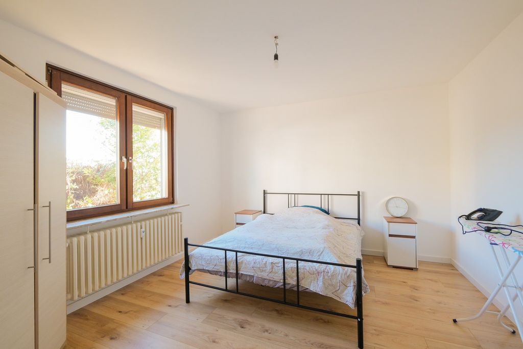 A simply furnished bedroom with a double bed, two nightstands, a large window, and an ironing board with an iron.