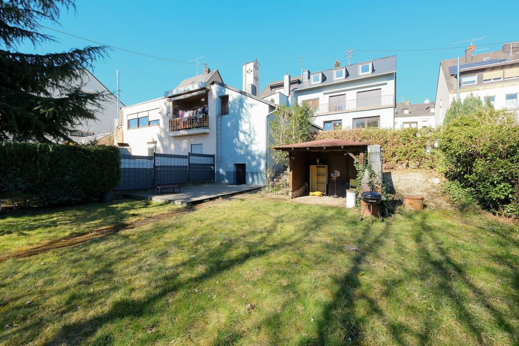 A spacious garden with green grass, surrounded by tall hedges and several residential buildings in the background under a clear sky.